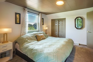 A bedroom with a bed, bedside lamps, a window with curtains, a door, and a wall-mounted mirror.