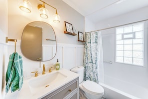 Une salle de bain avec un lavabo blanc, des robinets dorés, un miroir et une douche dotée d’une fenêtre en verre dépoli.