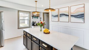 A kitchen with a large island, pendant lights, a refrigerator, and a window.