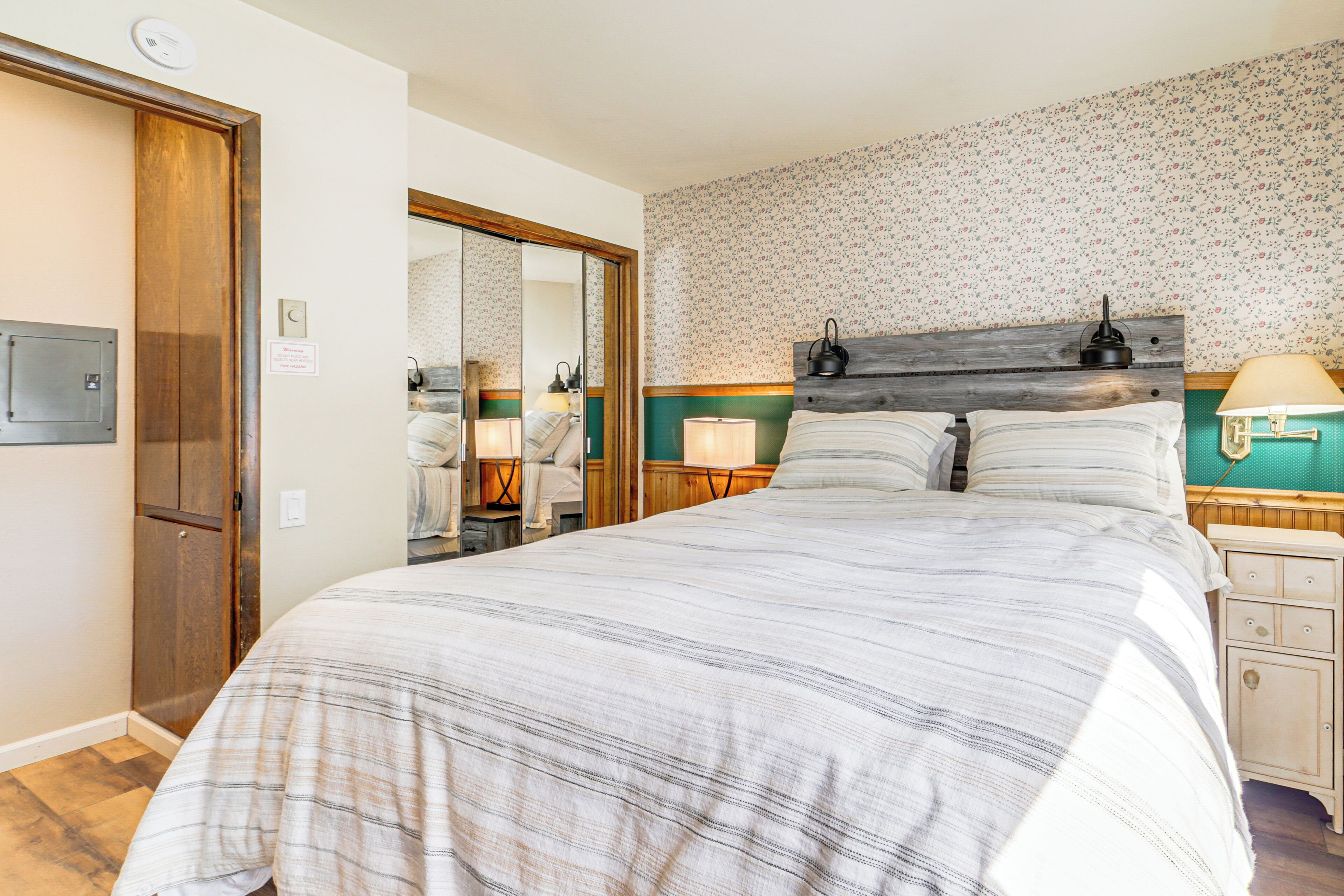 A bedroom with a large bed, wooden headboard, two bedside tables with lamps, a mirror, and a wardrobe.