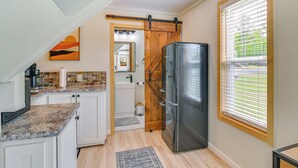 A kitchen with white cabinets, a granite countertop, a stainless steel refrigerator, and a window with blinds.