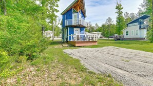 A blue cabin with a balcony, surrounded by trees and a gravel driveway.