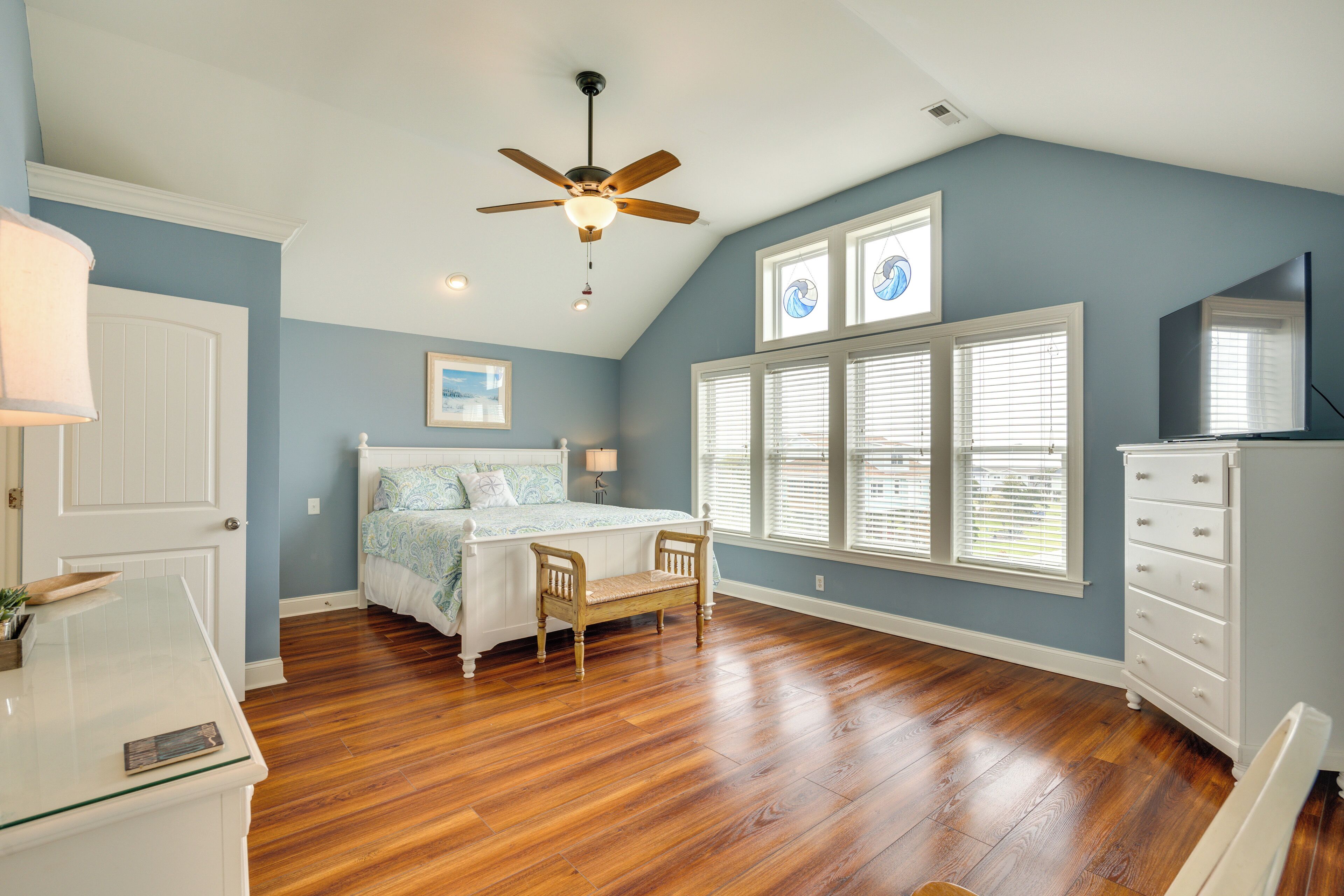 A bedroom with a bed, a wooden bench, a dresser, and a ceiling fan.