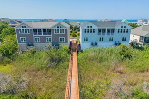 Un área residencial costera con casas de dos pisos, un paseo marítimo de madera y vista al océano.