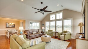 A spacious living room with a ceiling fan, a dining area with a chandelier, and large windows offering views.