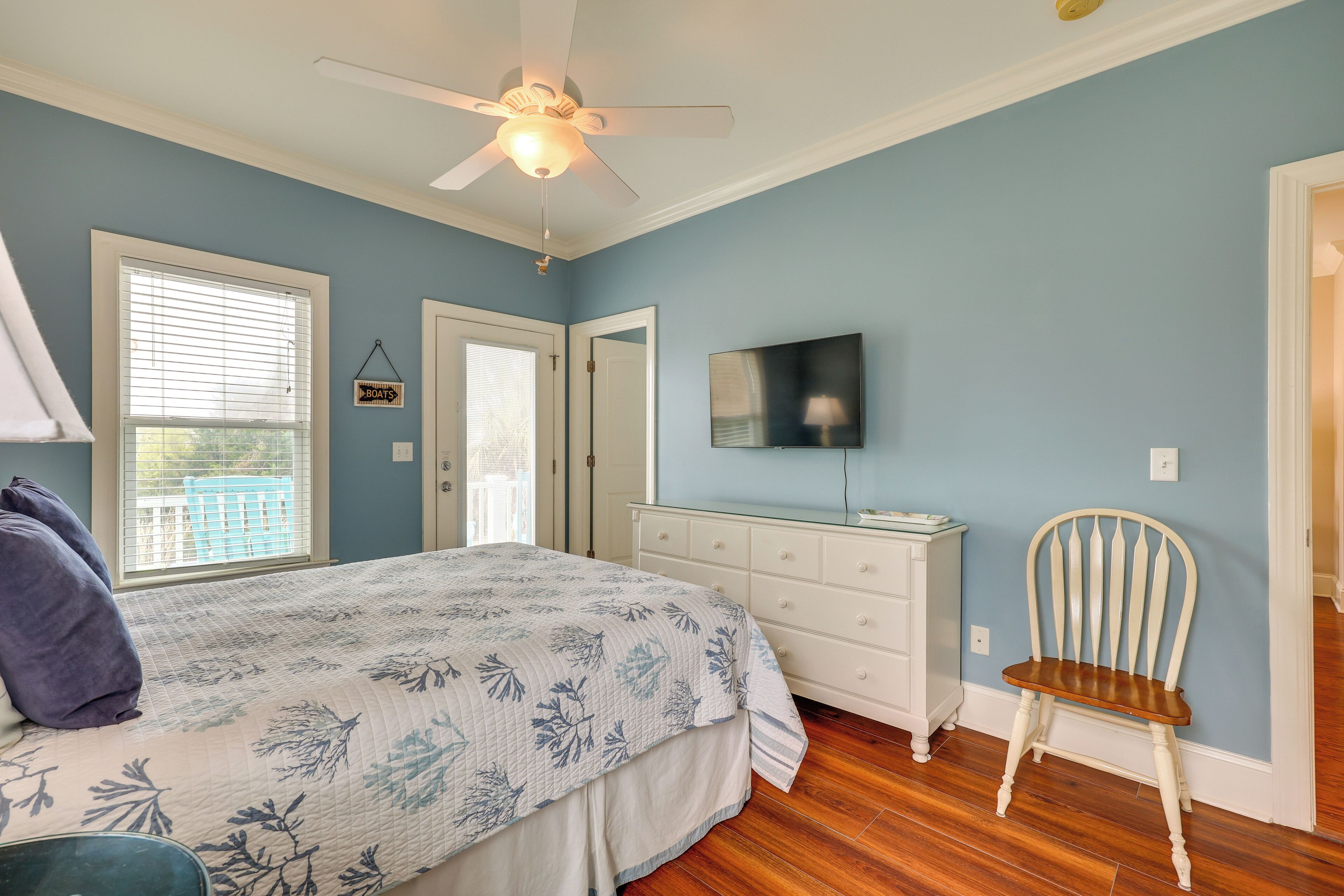A bedroom with a bed, a dresser, a chair, a ceiling fan, and a TV.