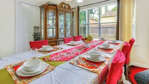 A dining room with a long table set for a meal, a wooden cabinet, and a window with a view of a house. - Home 7 Mi to Energy Corridor: Remote-work Ready! (Houston)