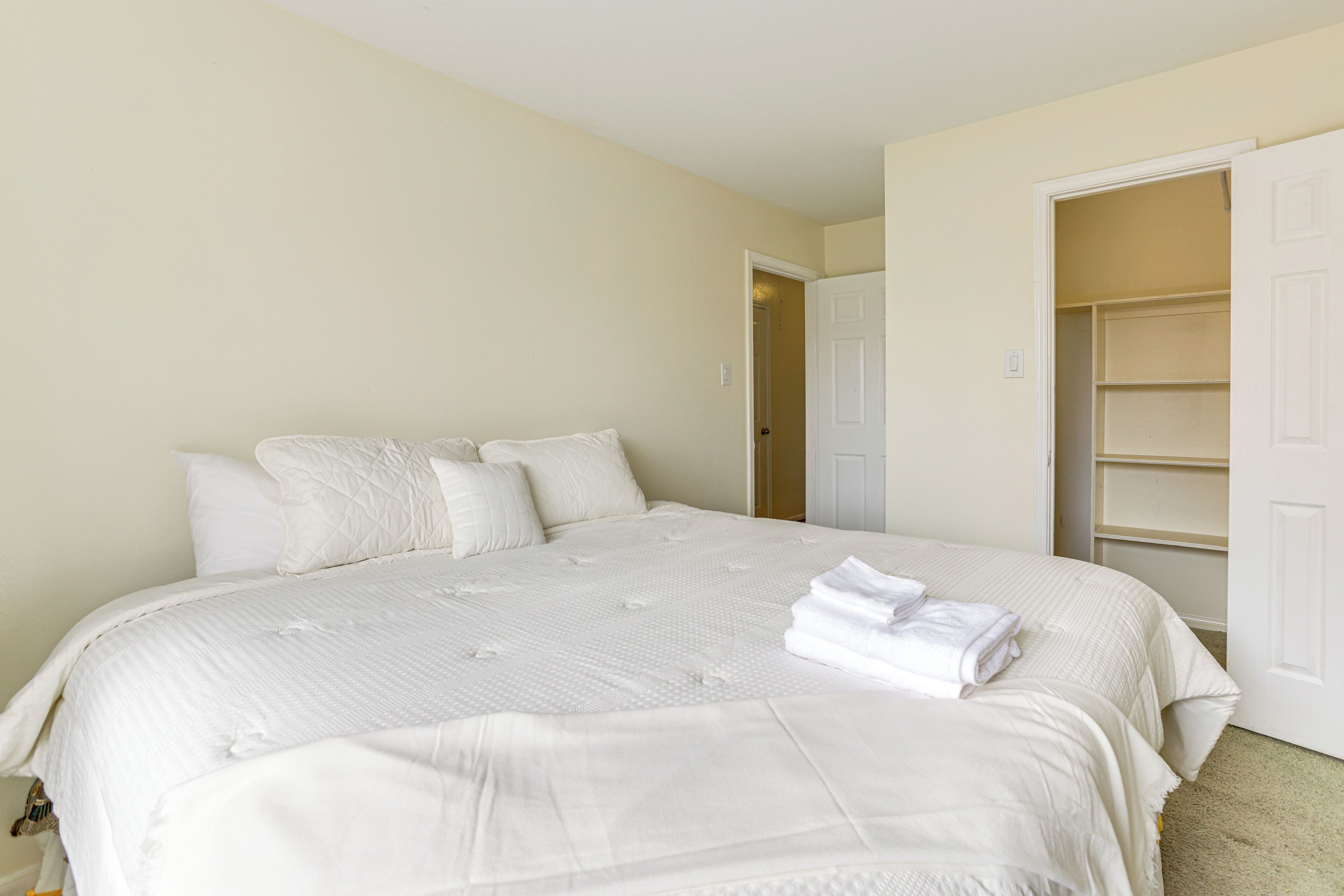 A neatly made bed with white linens and a folded towel on the side.