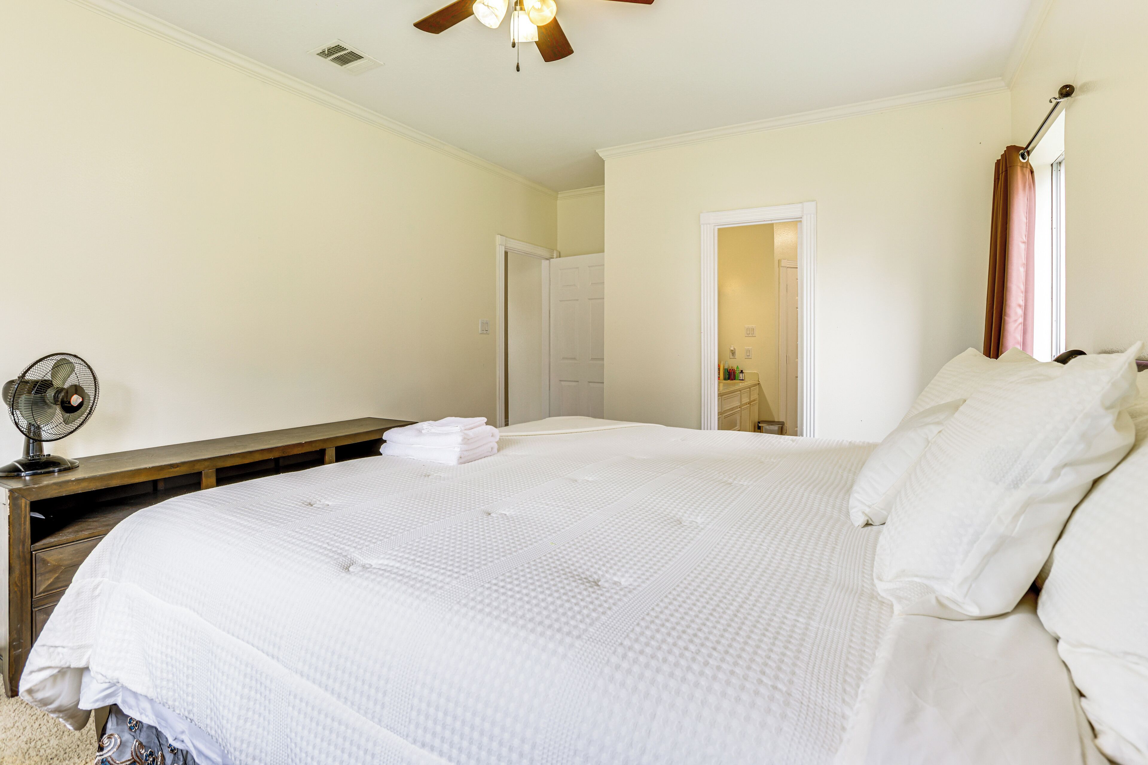 A bedroom with a large bed, a ceiling fan, and a wooden nightstand.