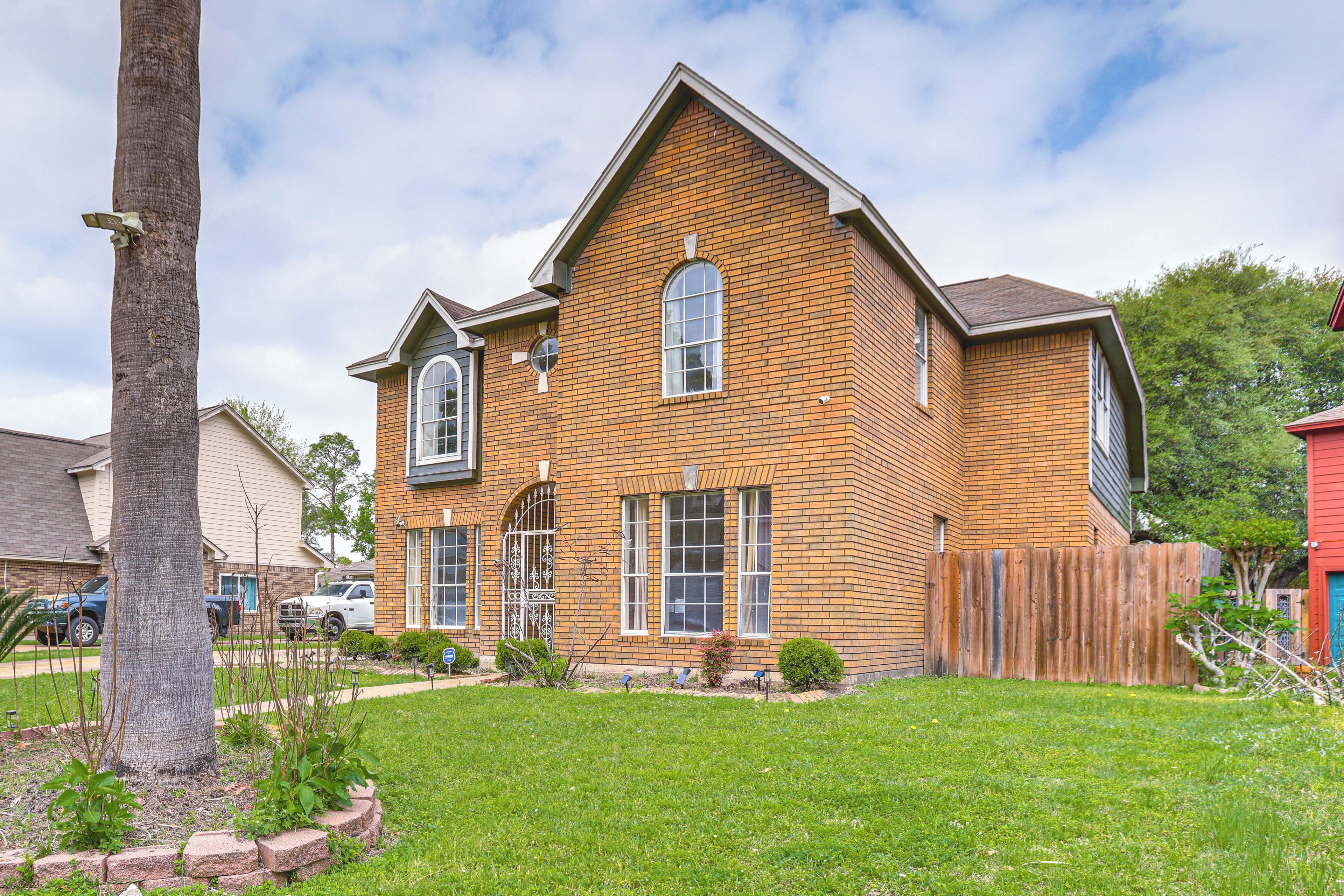 A two-story brick house with a front yard, a wooden fence, and a palm tree.