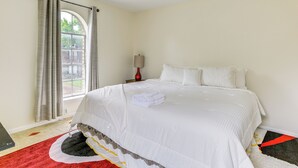 A bedroom with a large bed, a window with curtains, a nightstand with a lamp, and a red and black rug. - Home 7 Mi to Energy Corridor: Remote-work Ready! (Houston)
