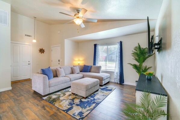 A living room with a sectional sofa, a ceiling fan, a large window with curtains, and a wooden floor. - 3 Mi to Riverside Park: Grants Pass Getaway! (Grants Pass)