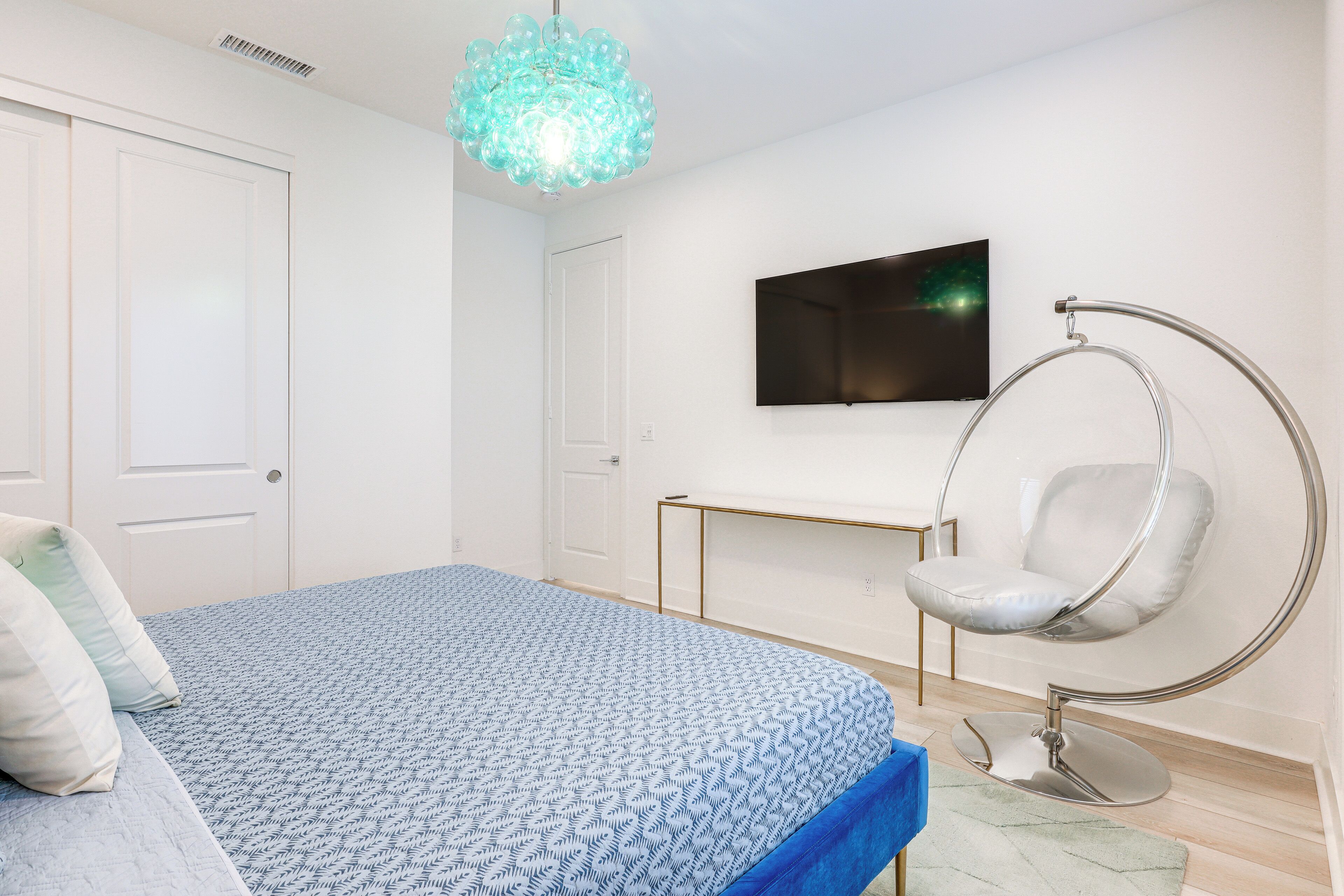 A bedroom with a bed, a hanging chair, a TV, and a door.