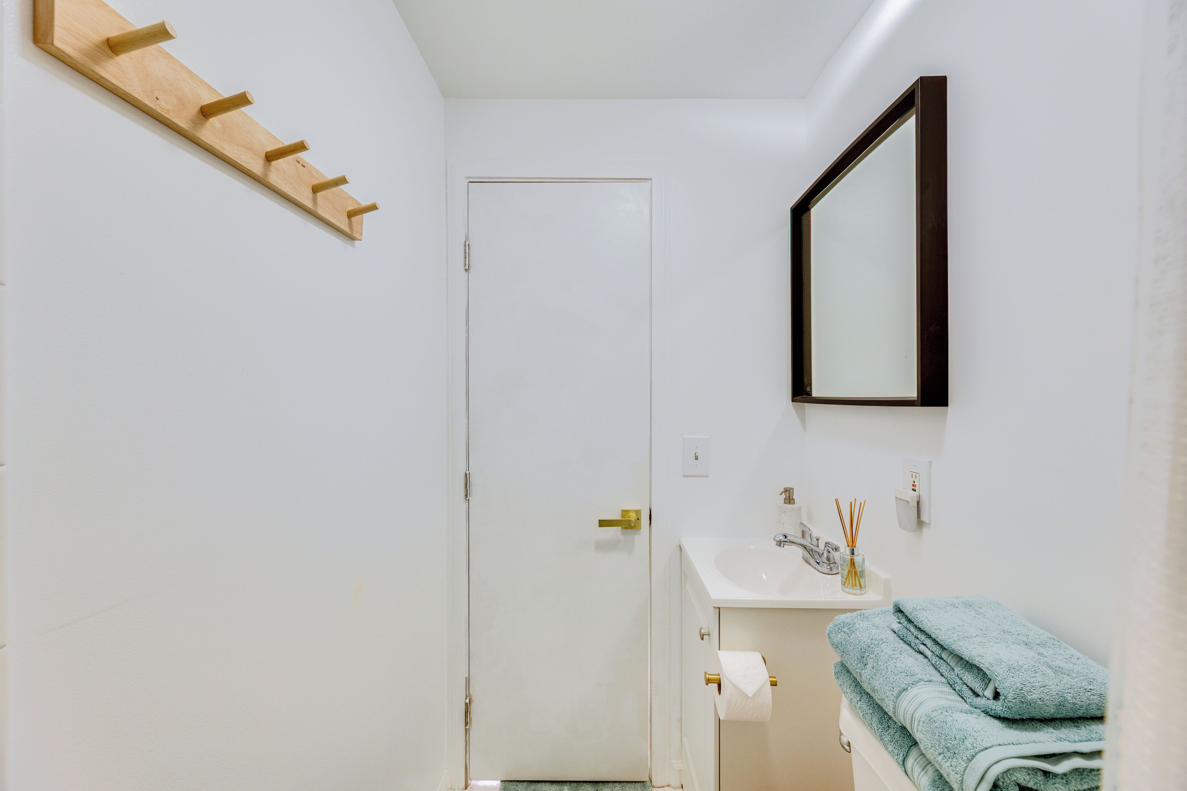 Une salle de bain avec une porte blanche, un lavabo avec un miroir et un porte-serviettes.