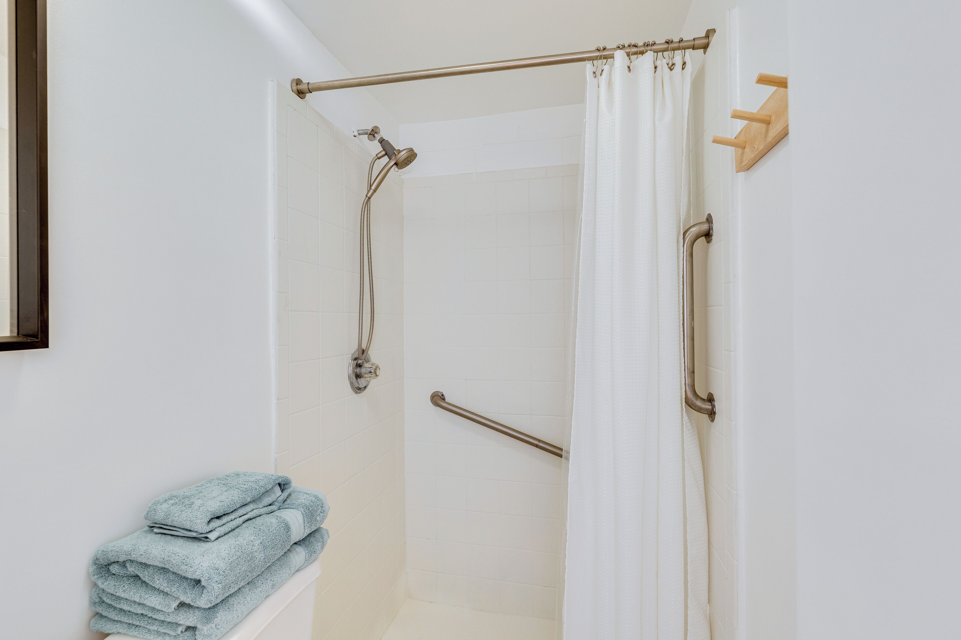 A shower area with a grab bar, a towel rack, and a shower curtain.