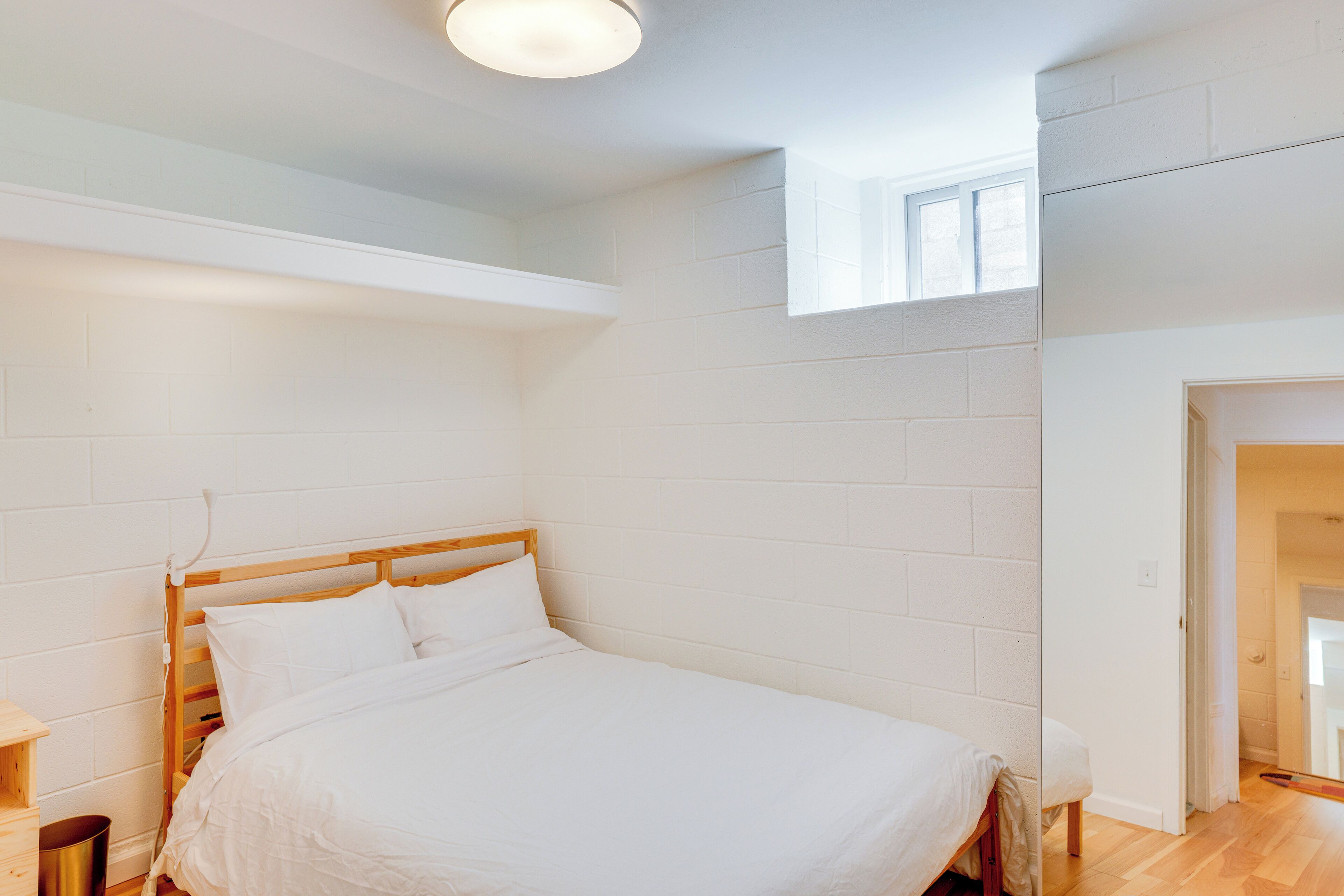 Un dormitorio con cama de madera, paredes blancas y tragaluz.