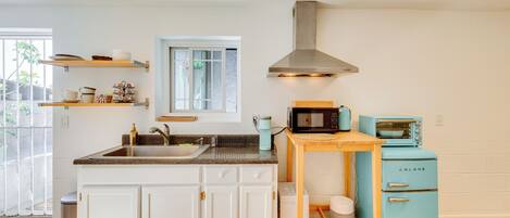 Cocina moderna con armarios blancos, encimera de granito, campana extractora de acero inoxidable, microondas verde azulado antiguo y un refrigerador pequeño.
