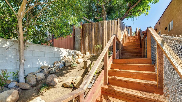 Un escalier en bois avec une rampe en métal, entouré de rochers et de plantes.