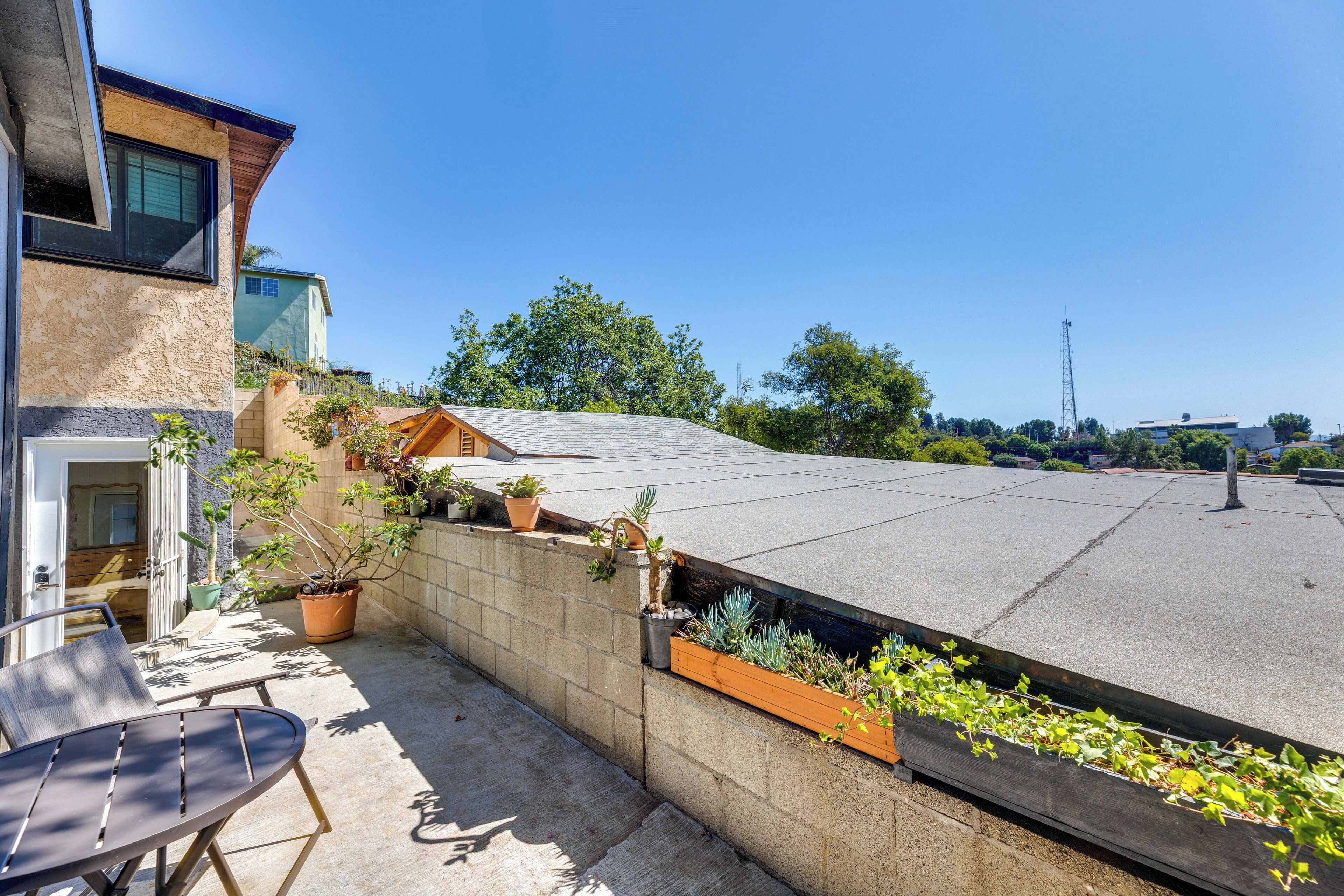 A rooftop patio with a concrete floor, a wooden bench, and potted plants.