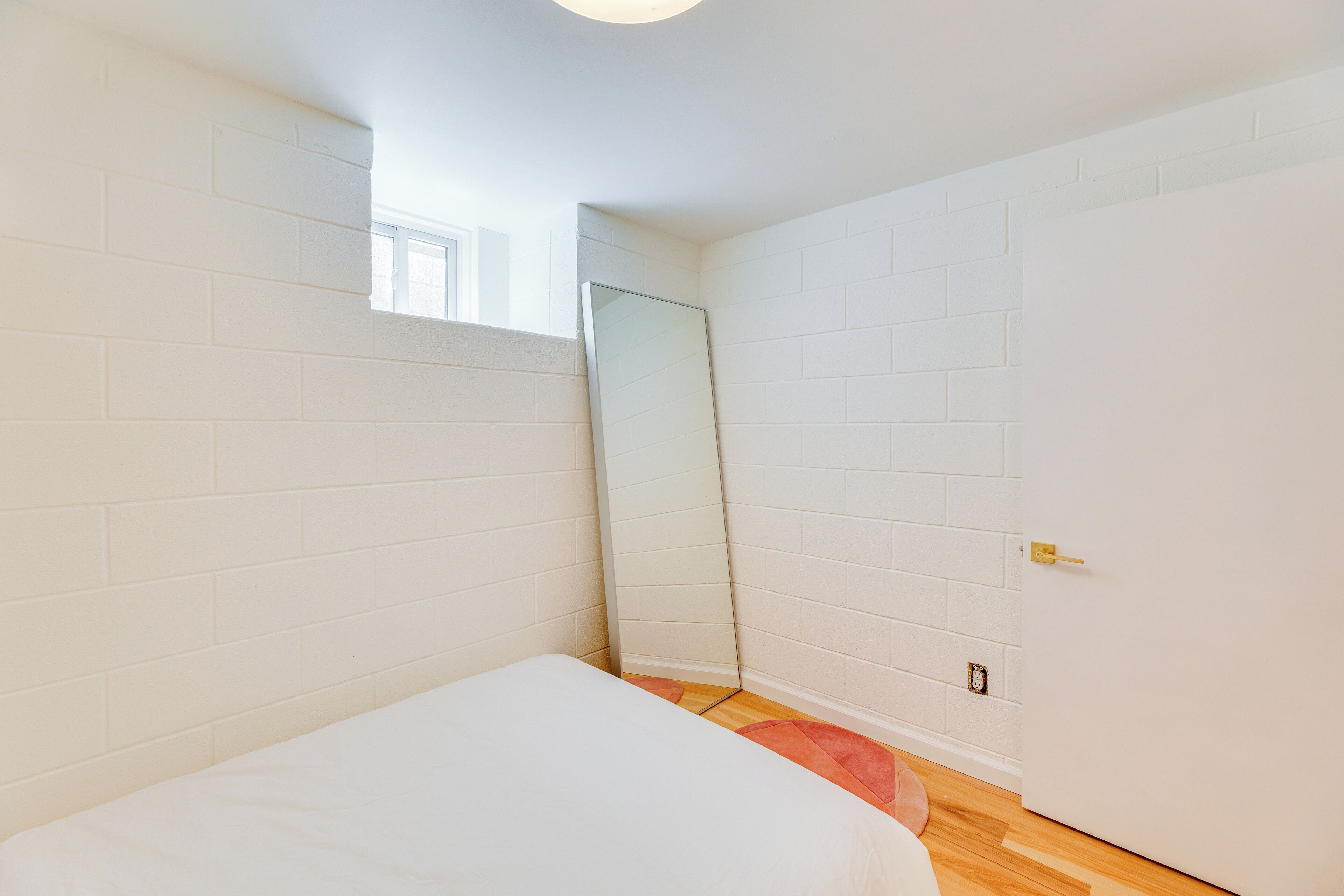 Un dormitorio con paredes de ladrillo blanco, una cama, un espejo grande y una puerta.