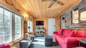 A cozy log cabin interior with a red sofa, a small table, and a television mounted on the wall. - 2 Mi to Ossipee Lake: Forest-view Sanctuary! (Freedom)
