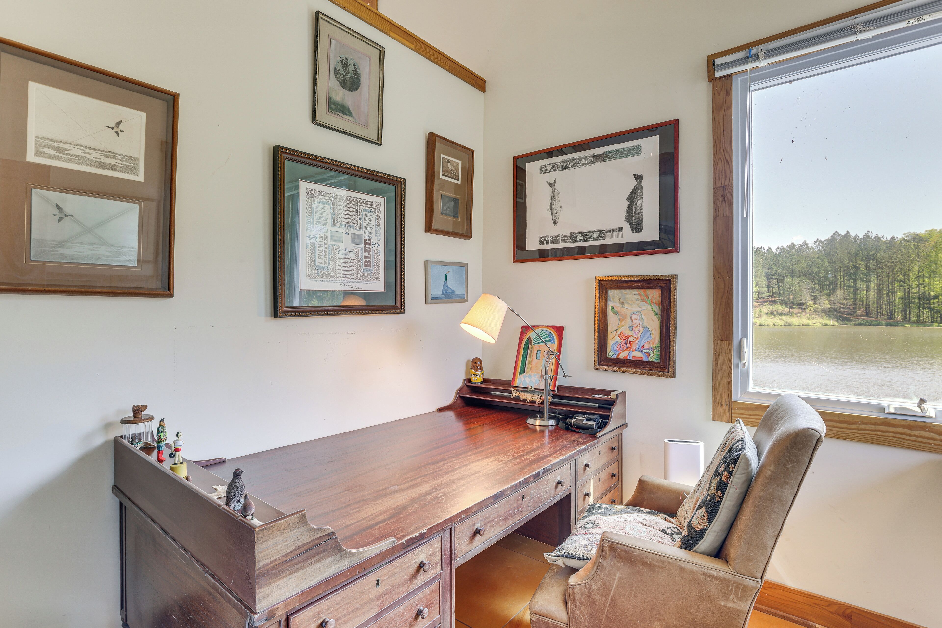 Een kamer met een houten bureau, een stoel en een raam met uitzicht op een meer.
