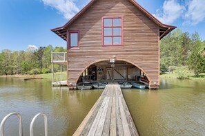 A wooden cabin with a dock extending into a lake, featuring a covered boat launch area and several boats. - 2 Docks + Paddleboard: Lakefront Alabama Retreat! (Trussville)