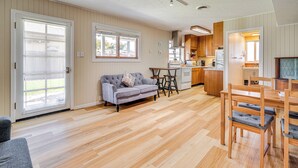 Un amplio salón con suelo de madera, un sofá gris, una mesa de comedor con sillas y una cocina al fondo.