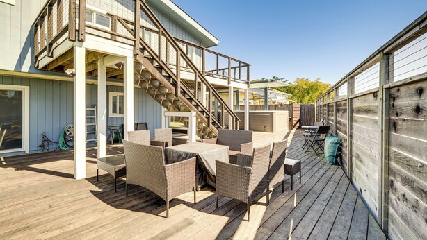 Una terraza de madera con mobiliario exterior, una escalera y una zona de estar cubierta.