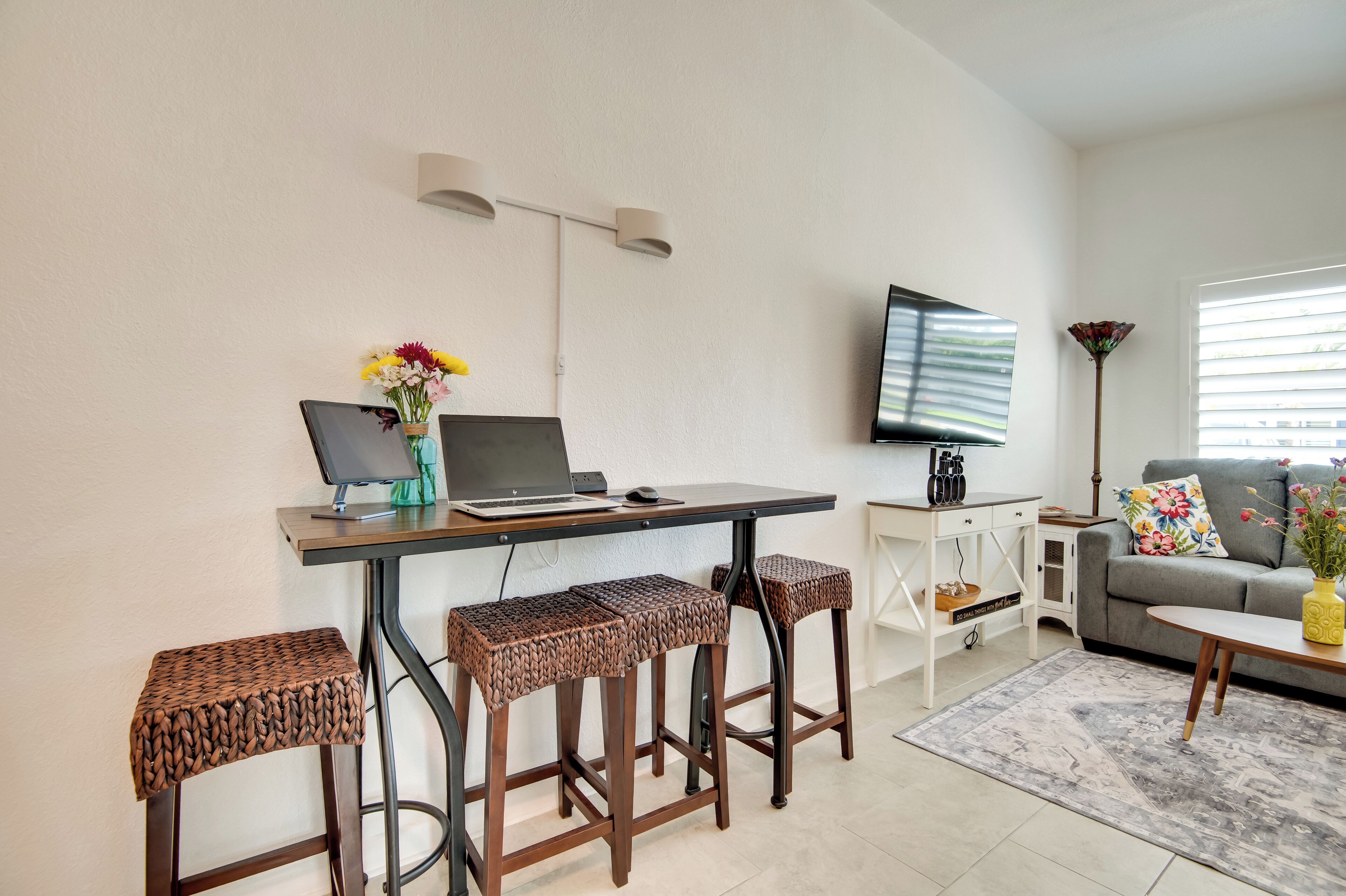 Un salon moderne comprenant un coin repas, un téléviseur à écran plat fixé au mur et un canapé agrémenté d’un coussin à motifs floraux.