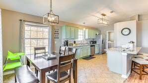 A spacious kitchen with light green cabinets, a central island, and a dining area with wooden chairs and a table. - Outdoor Entertaining Space: Family Home in Milton (Milton)