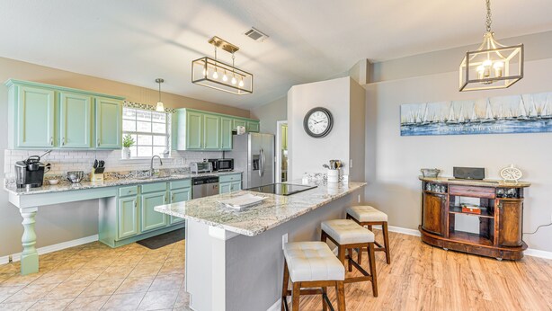 A spacious kitchen with teal cabinets, a large island with stools, and a wooden sideboard. - Outdoor Entertaining Space: Family Home in Milton (Milton)