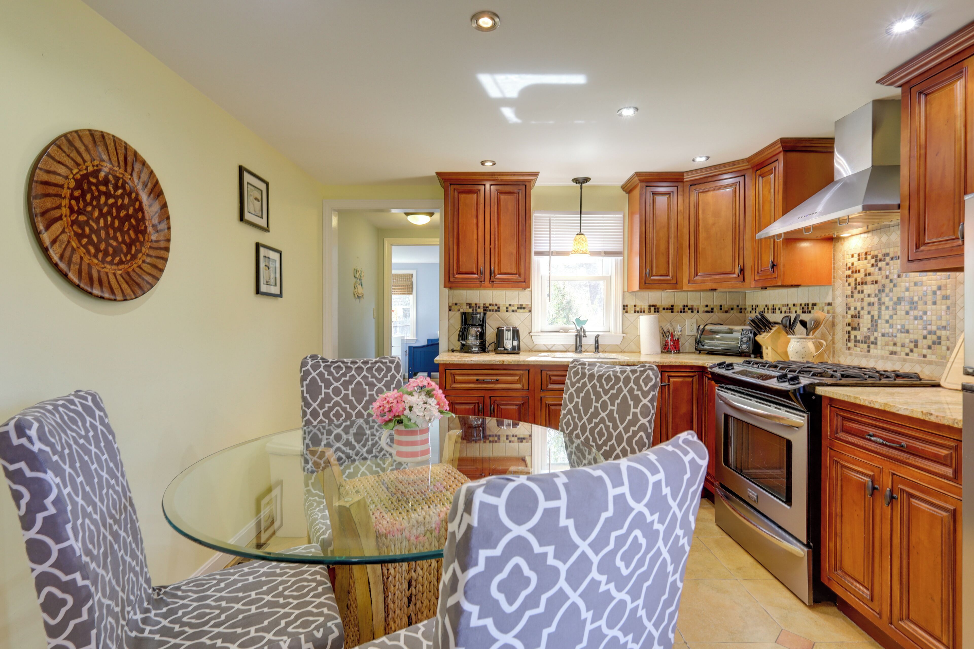 A kitchen with wooden cabinets, a glass dining table, and patterned chairs.