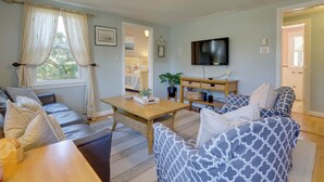 A living room with a sofa, a patterned armchair, a wooden coffee table, and a television on the wall. - 1 Mi to South Village Beach: Bbq-ready Retreat (West Dennis)