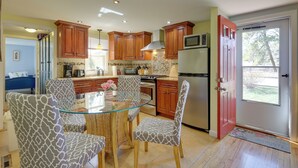 A modern kitchen with wooden cabinets, a glass dining table, and patterned chairs. - 1 Mi to South Village Beach: Bbq-ready Retreat (West Dennis)