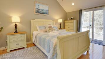 A bedroom with a bed, two bedside tables, a dresser, a painting, and a large window.