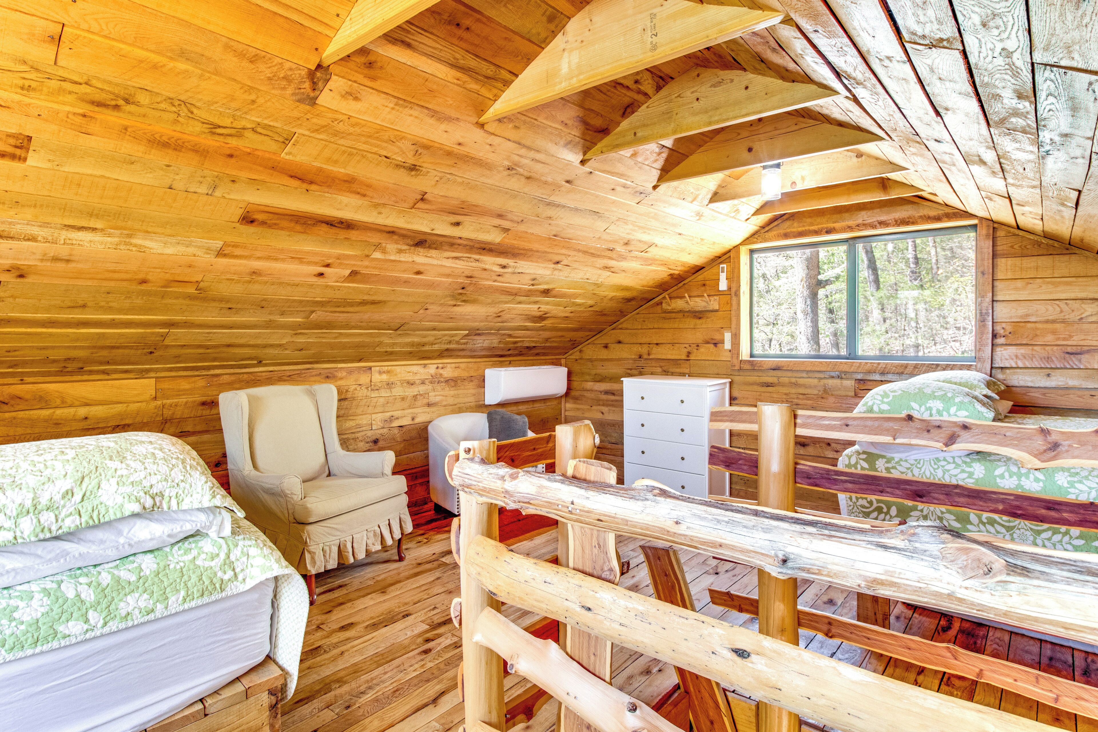 Una cabaña con interior de madera, una cama, una silla, un aparador y una ventana con vista a un bosque.