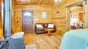 Un accogliente interno di una baita di legno con camino, divano, tavolo e letto.