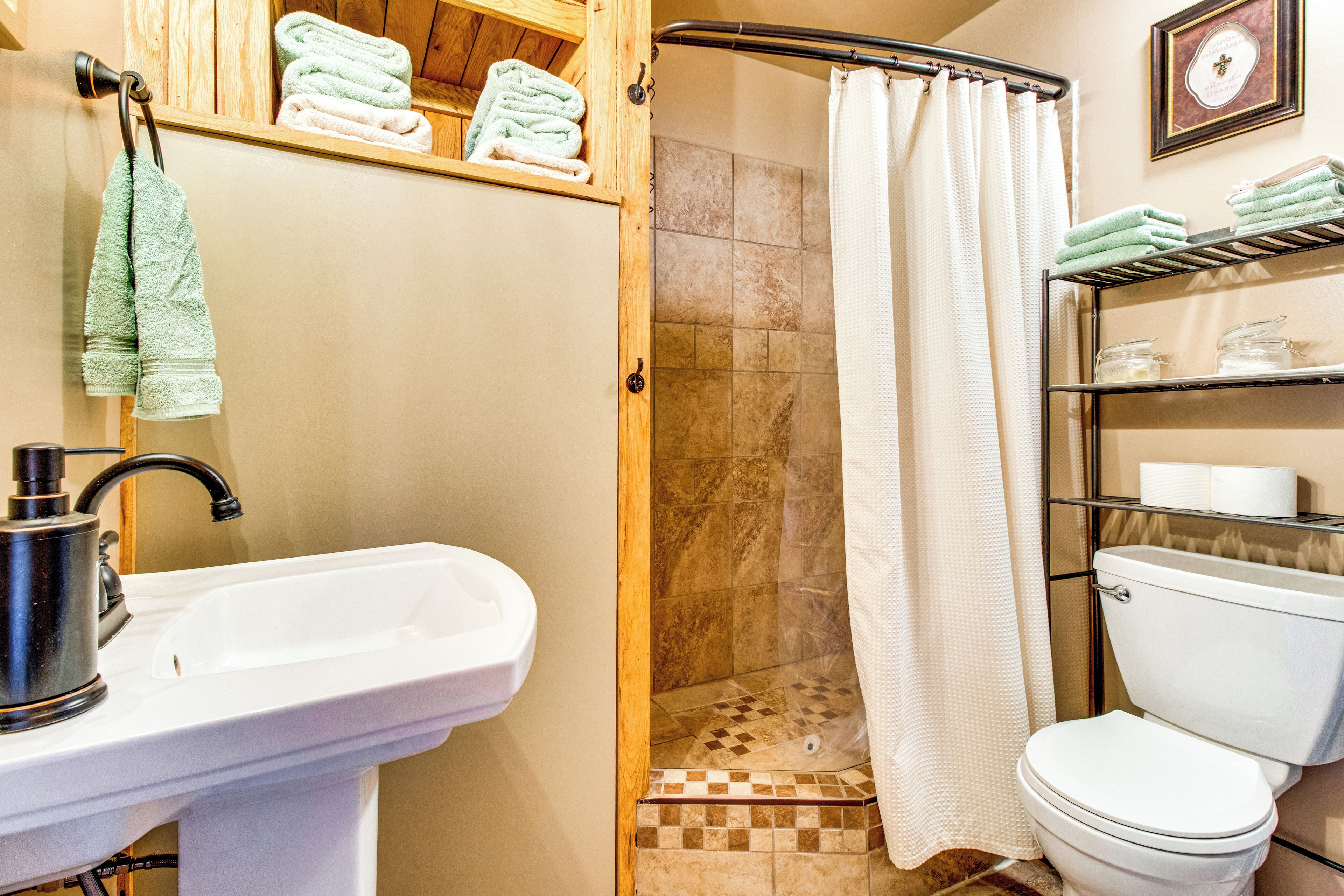 A bathroom with a sink, toilet, shower, and shelves with towels.