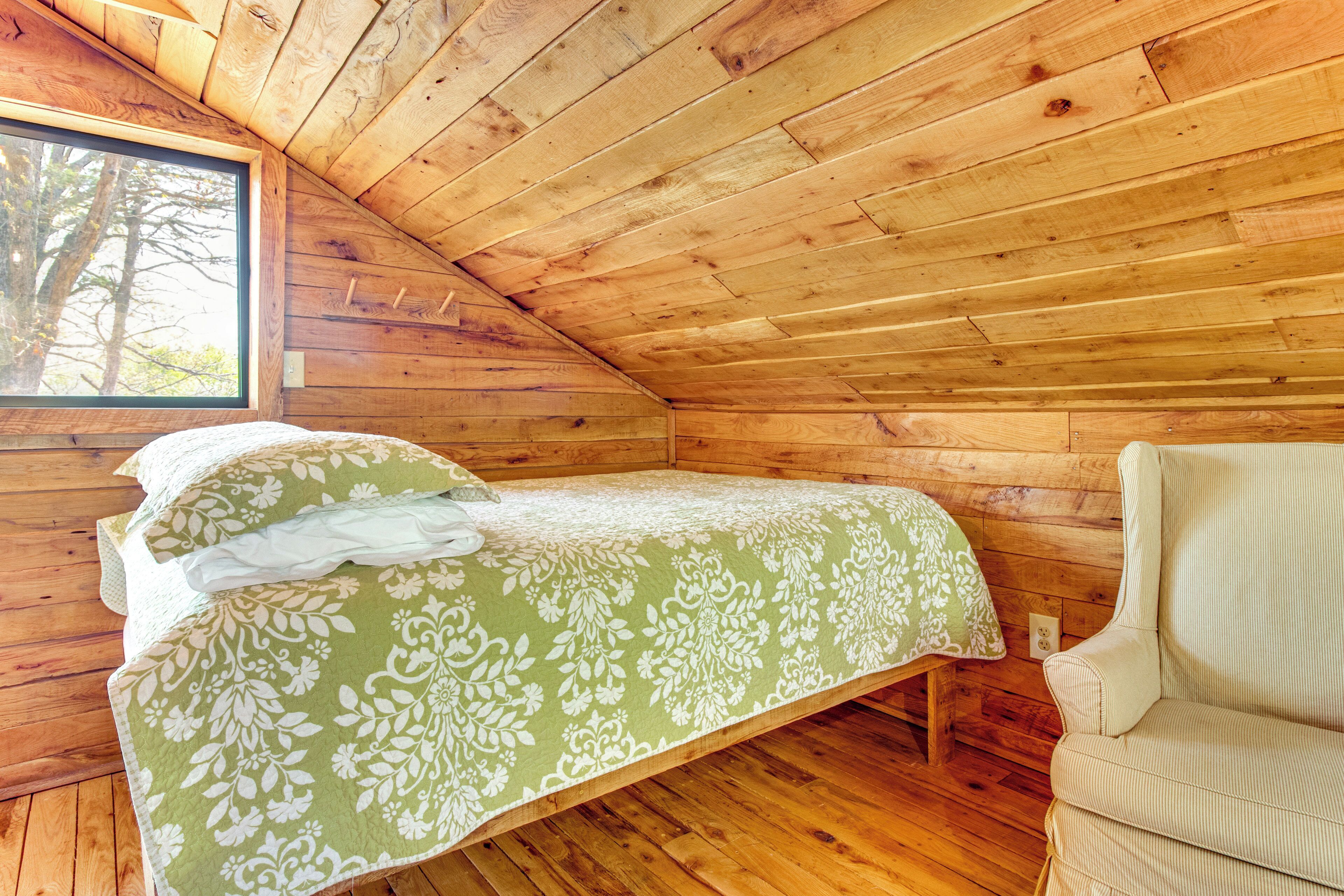 A wooden cabin room with a bed, a chair, and a window.