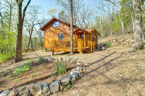 Una baita di legno con veranda, circondata da alberi e un vialetto sterrato.
