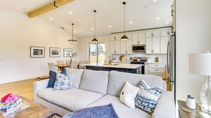 A modern living room with a grey sofa, blue and white patterned cushions, a wooden coffee table, and a clear acrylic tray with flowers. - Patio + Outdoor Dining: Modern Home in Paradise (Paradise)