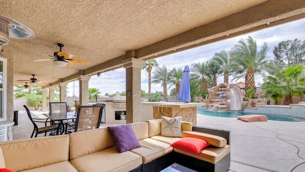 Uma área de pátio externa com sofá, cadeiras, mesa, piscina e palmeiras.