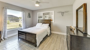 A bedroom with a bed, a ceiling fan, a window with curtains, a dresser, and a mirror. - Waterfront Retreat w/ Pool & Yard in Sarasota (Sarasota)