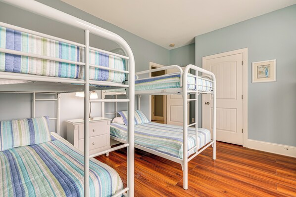 Een slaapkamer met een stapelbed, houten vloer, witte muren en een deur.