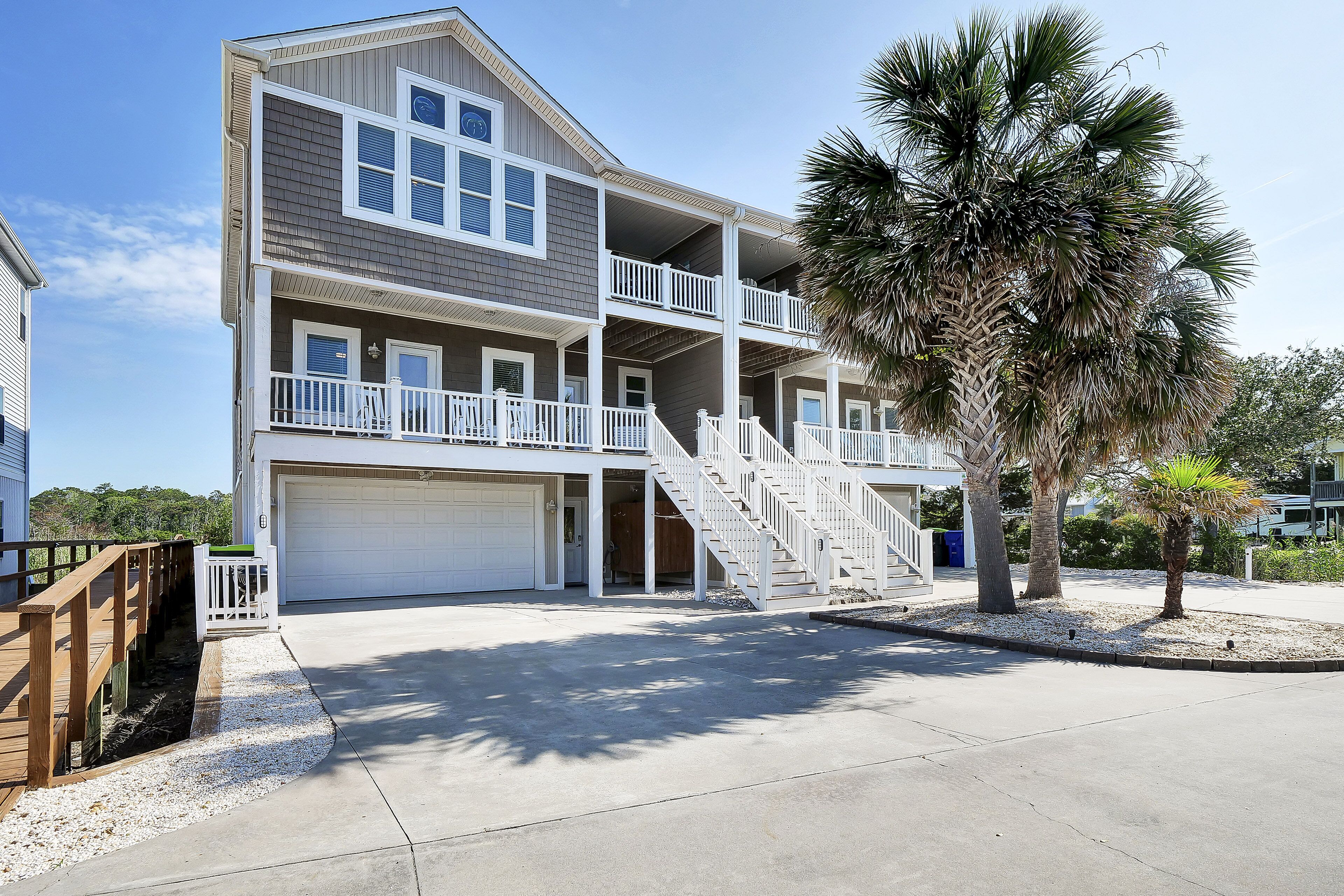 A multi-story residential building with a two-story balcony, a garage, and a palm tree in the foreground.