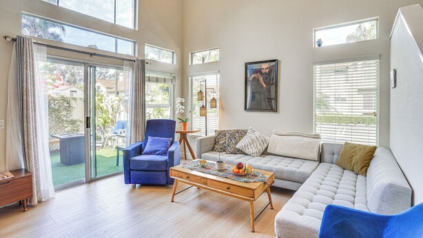 Uma sala de estar espaçosa com um sofá, poltronas e uma mesa de centro. Há grandes janelas e uma porta de vidro deslizante que dá para um pátio.