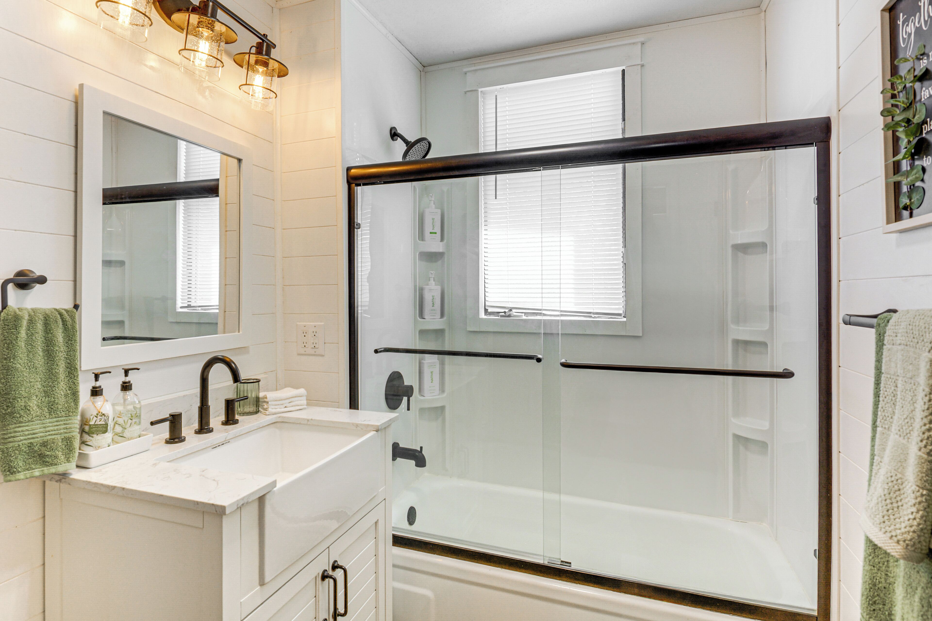 Un bagno moderno con cabina doccia in vetro, uno specchio grande e un lavandino bianco con articoli da toilette.