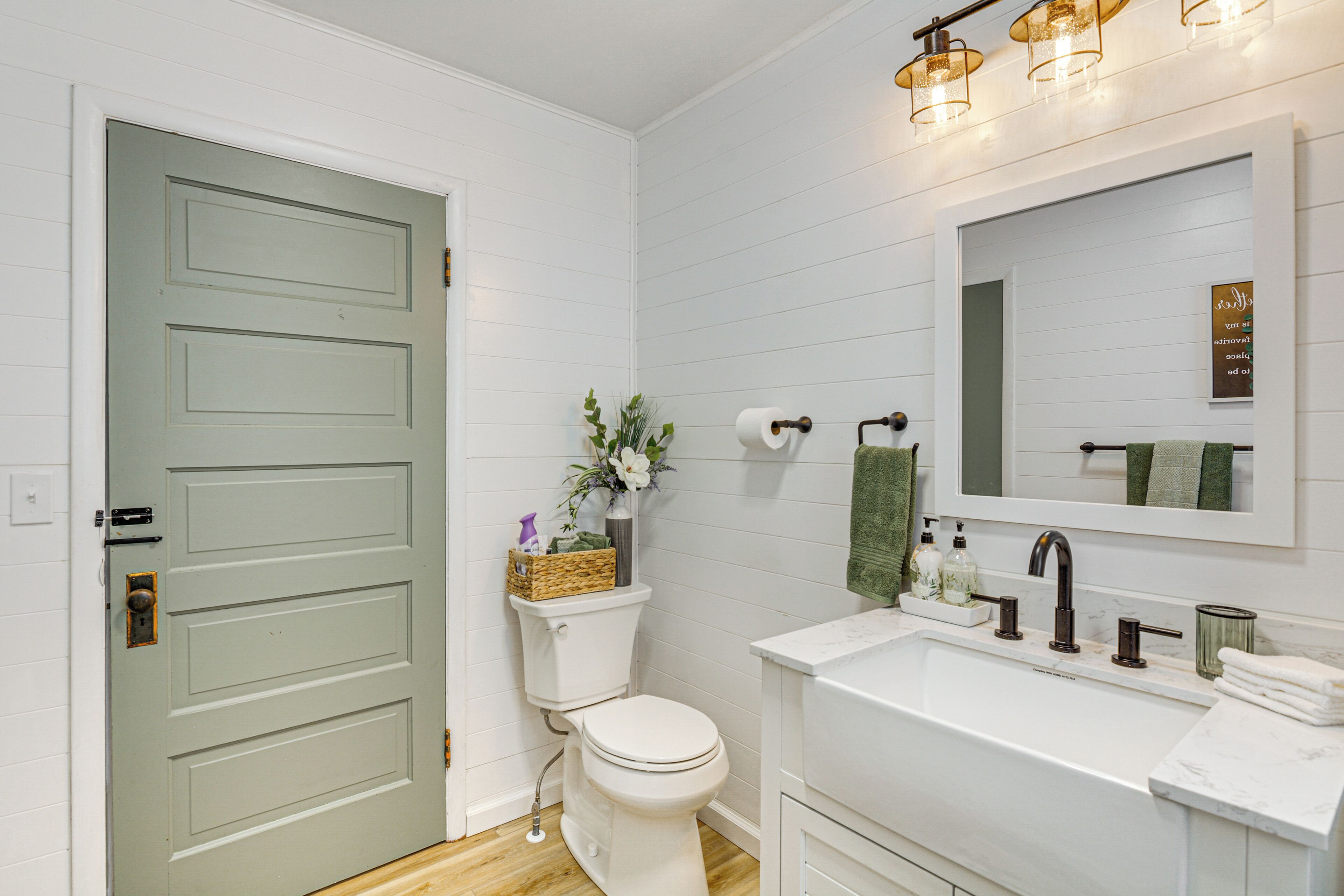 Une salle de bain avec un lavabo blanc, des toilettes et une porte verte.
