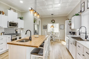 Una cocina moderna con armarios blancos, una isla de madera con un lavamanos e iluminación colgante.
